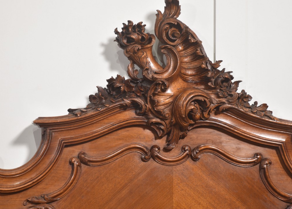 A matching pair of carved walnut single bed frames with high crest headboards, serpentine footboards, and book-matched timber panels. View IV