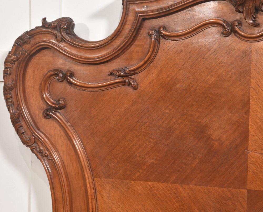 A matching pair of carved walnut single bed frames with high crest headboards, serpentine footboards, and book-matched timber panels. View VI