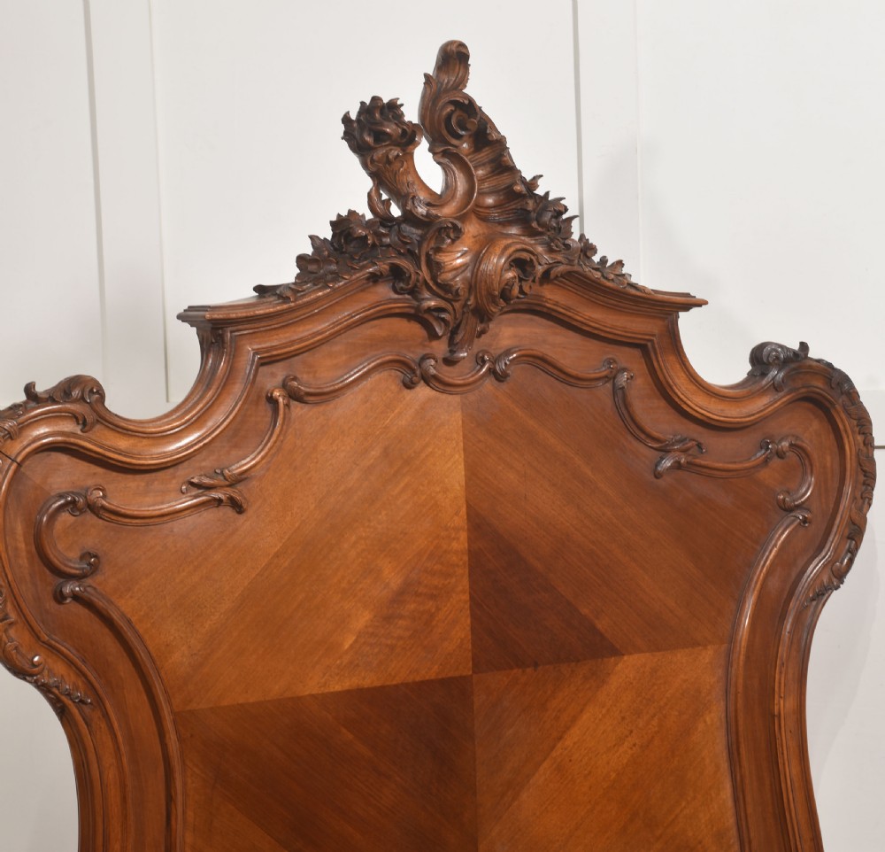 A matching pair of carved walnut single bed frames with high crest headboards, serpentine footboards, and book-matched timber panels. View VII
