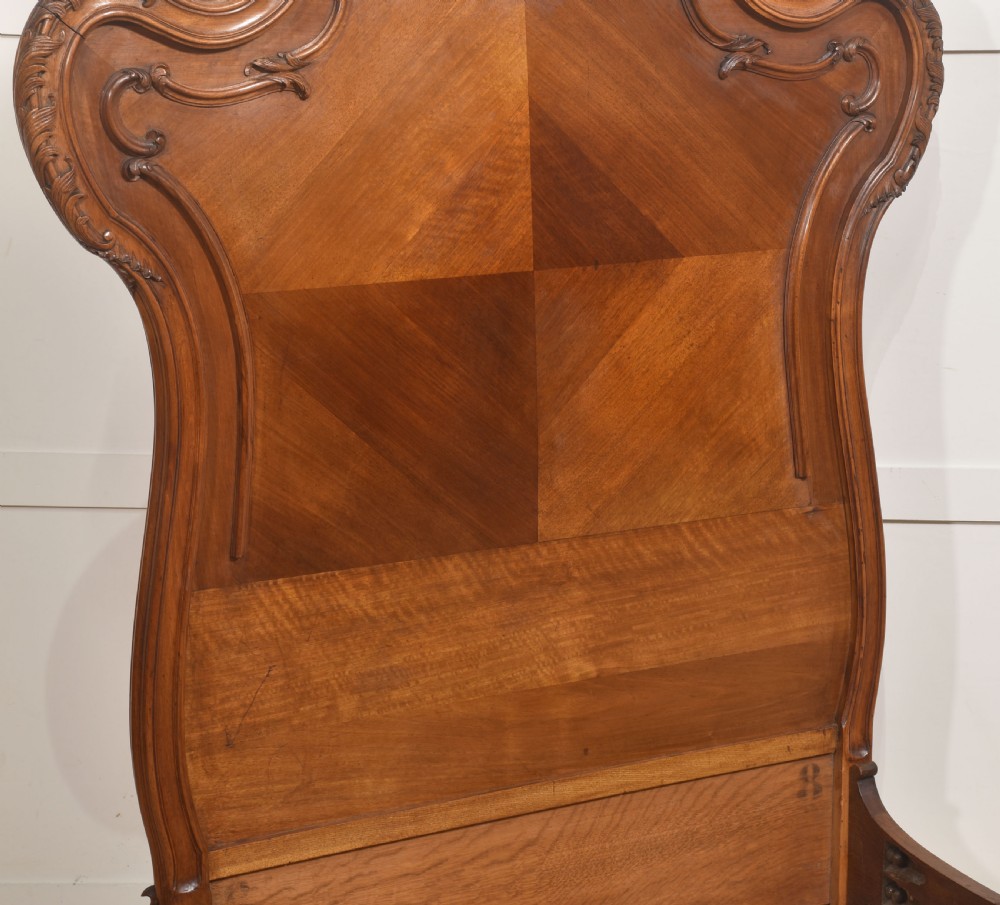 A matching pair of carved walnut single bed frames with high crest headboards, serpentine footboards, and book-matched timber panels. View VIII