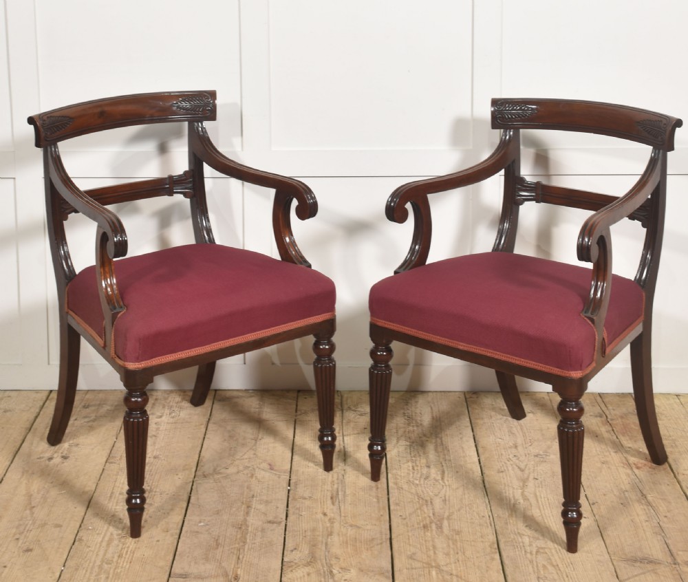 A pair of George IV mahogany armchairs featuring carved curved crest rails, swept arm supports, reeded front legs, and red fabric seats.