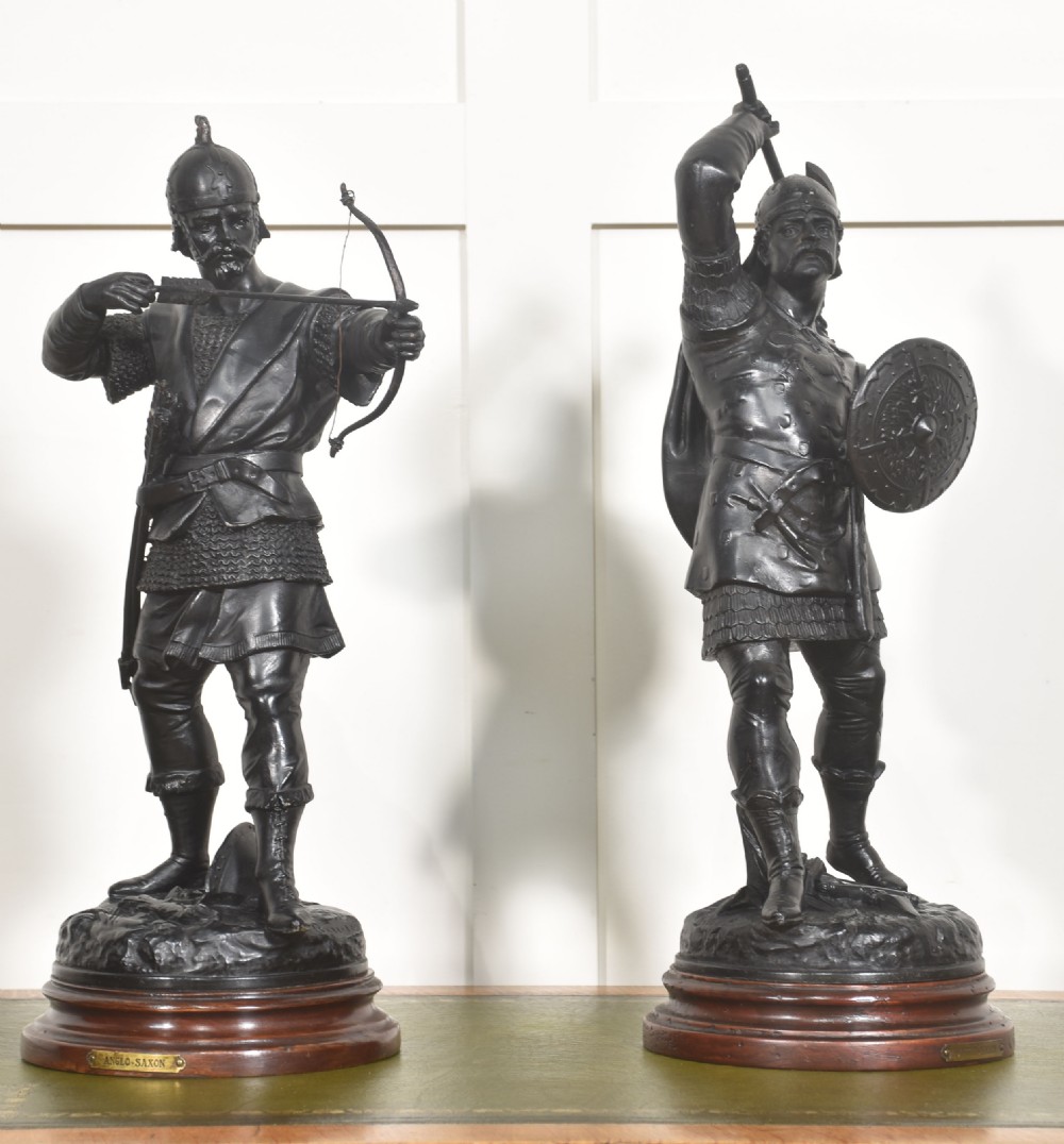 A pair of dark bronzed metal figures depicting Anglo-Saxon warriors, one drawn with a bow and the other raising an axe, mounted on circular wooden bases. View V