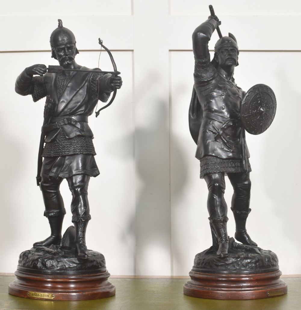 A pair of dark bronzed metal figures depicting Anglo-Saxon warriors, one drawn with a bow and the other raising an axe, mounted on circular wooden bases. View VI