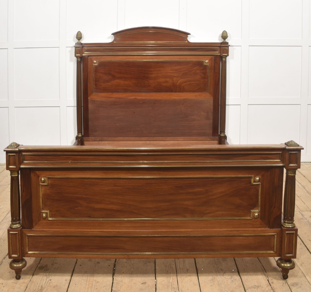 Late nineteenth-century mahogany bedframe featuring brass mouldings, fluted post columns topped with pineapple finials, and raised panel work on the headboard and footboard.