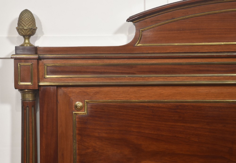 Late nineteenth-century mahogany bedframe featuring brass mouldings, fluted post columns topped with pineapple finials, and raised panel work on the headboard and footboard. View V