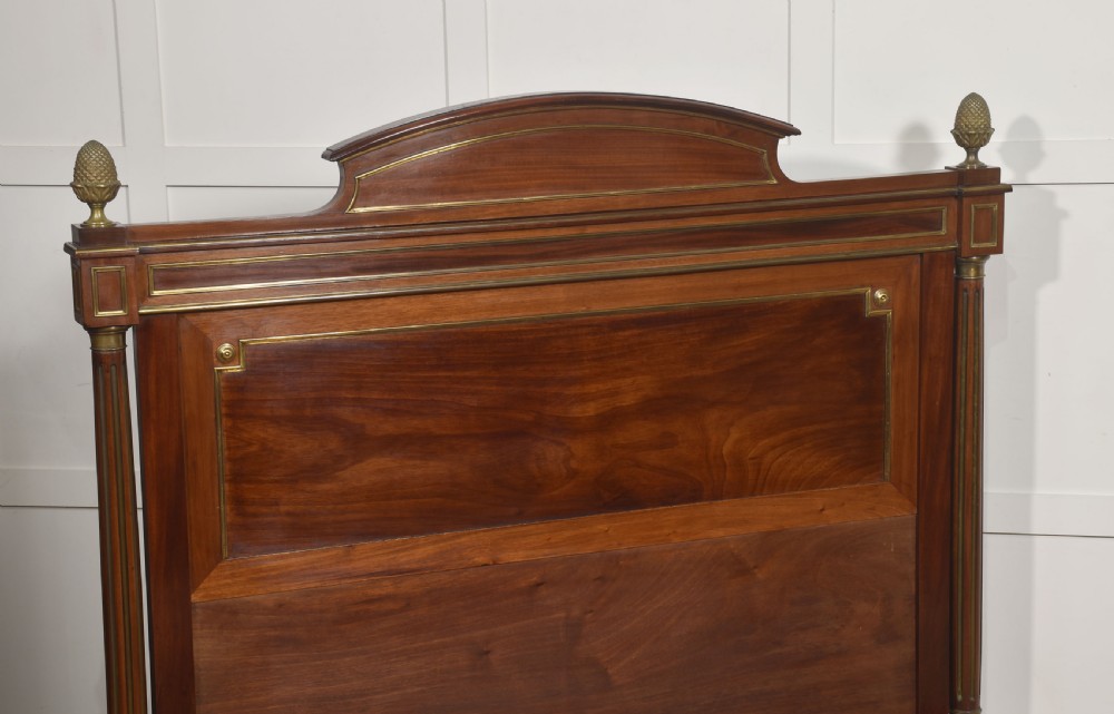 Late nineteenth-century mahogany bedframe featuring brass mouldings, fluted post columns topped with pineapple finials, and raised panel work on the headboard and footboard. View X