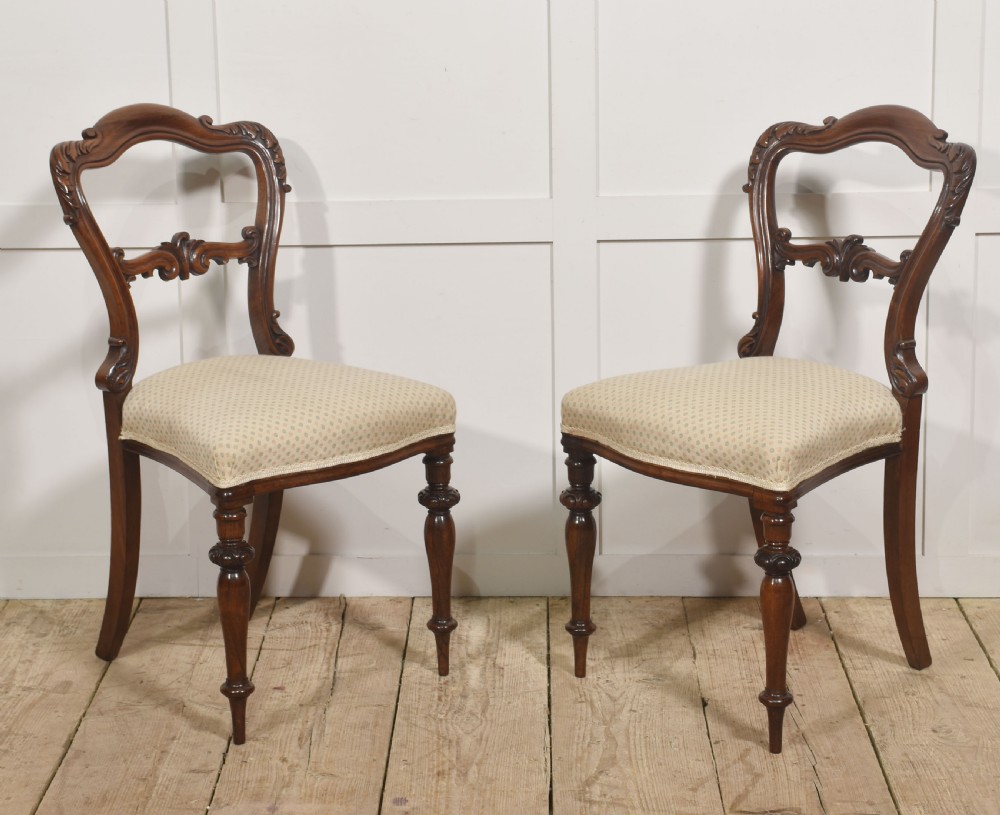 A pair of mid-19th-century rosewood side chairs featuring open balloon backs with carved detail rails, turned front legs, and cream-coloured patterned fabric seats.
