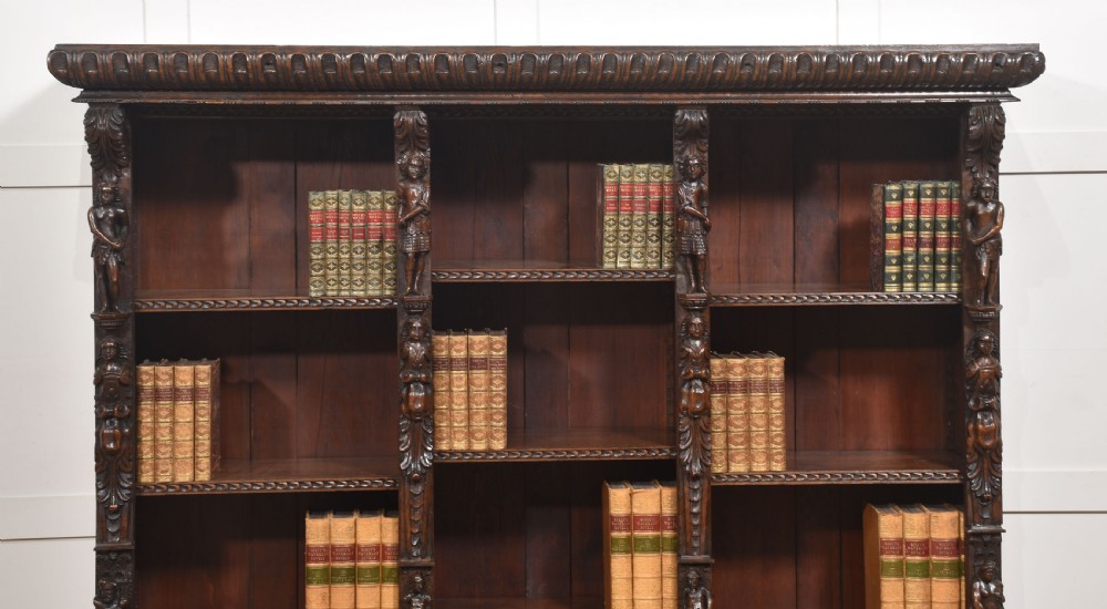 A late 19th-century carved oak open bookcase featuring three vertical bays, carved figures along the stiles, and decorative egg-and-dart moulding along the top cornice. View II
