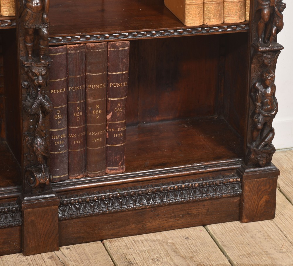 A late 19th-century carved oak open bookcase featuring three vertical bays, carved figures along the stiles, and decorative egg-and-dart moulding along the top cornice. View IV