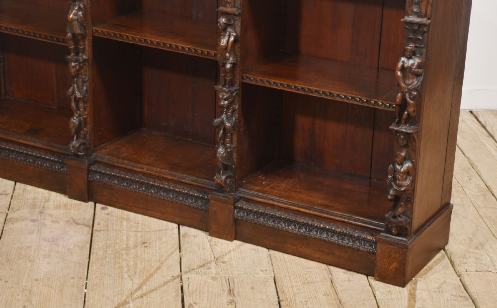 A late 19th-century carved oak open bookcase featuring three vertical bays, carved figures along the stiles, and decorative egg-and-dart moulding along the top cornice. View XVI