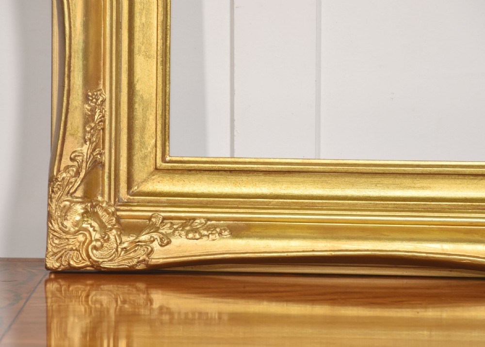 An ornate rectangular giltwood picture frame in the Rococo style featuring decorative corner mouldings and swept edges. View II