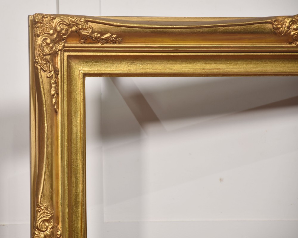 An ornate rectangular giltwood picture frame in the Rococo style featuring decorative corner mouldings and swept edges. View III