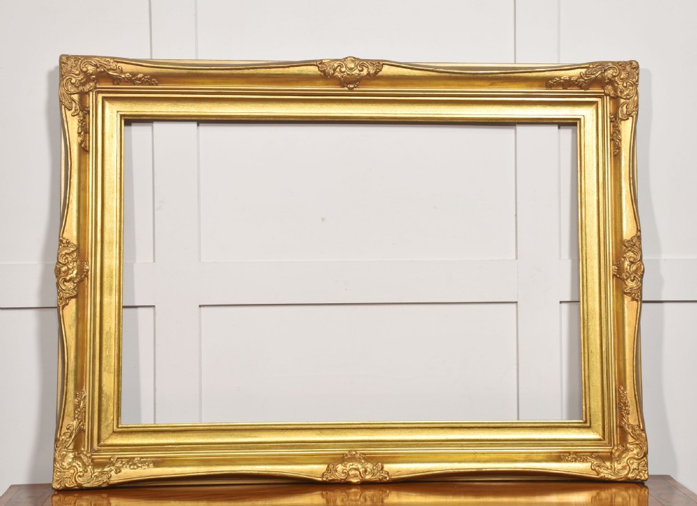 An ornate rectangular giltwood picture frame in the Rococo style featuring decorative corner mouldings and swept edges. View IV