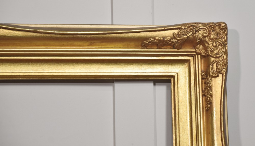 An ornate rectangular giltwood picture frame in the Rococo style featuring decorative corner mouldings and swept edges. View V