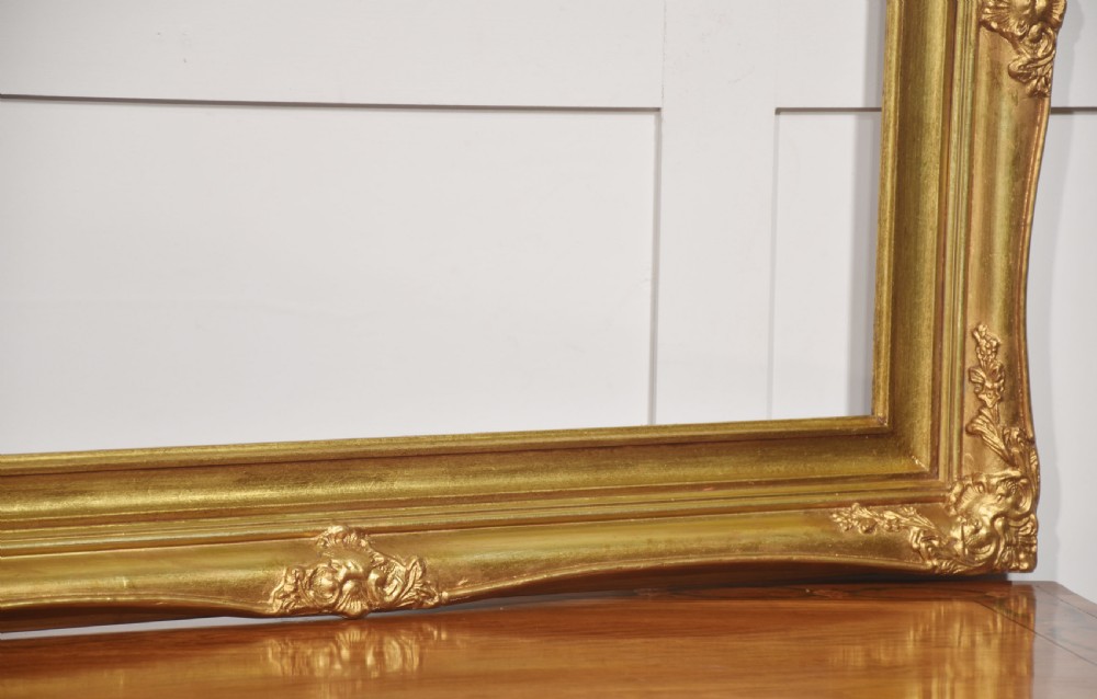 An ornate rectangular giltwood picture frame in the Rococo style featuring decorative corner mouldings and swept edges. View VI