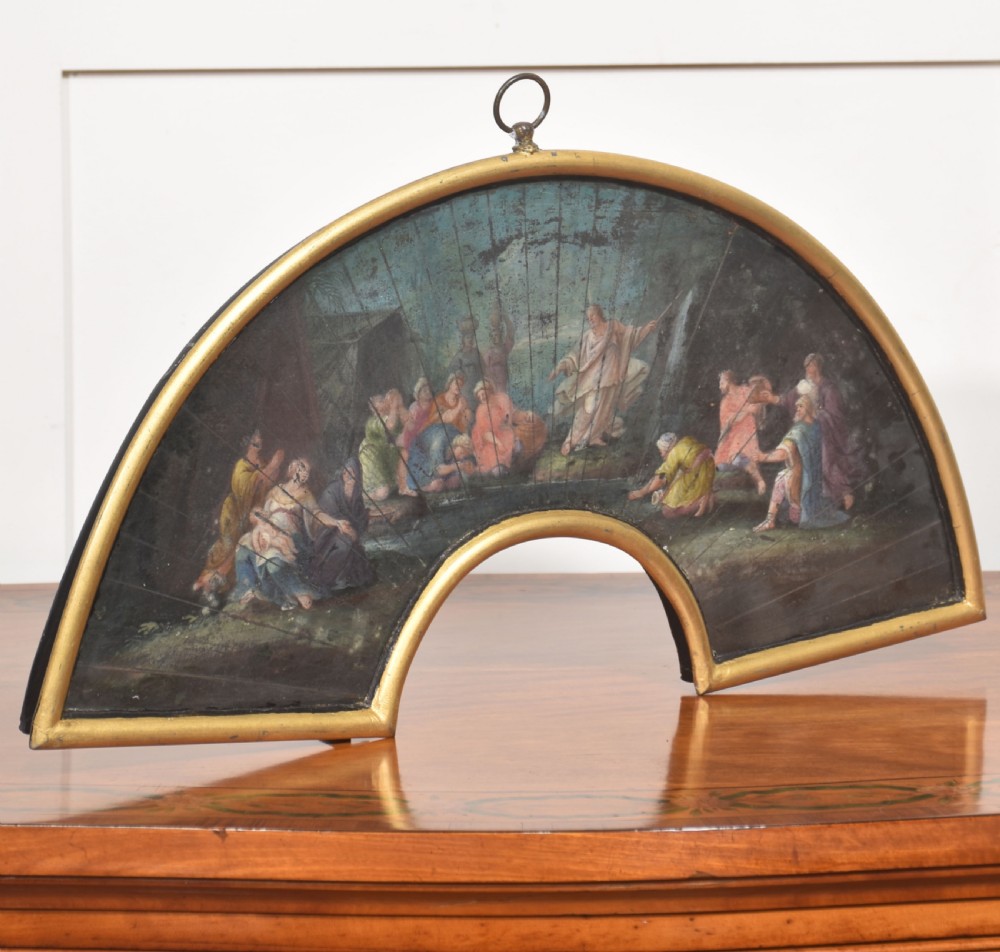 A fan-shaped gilt metal frame containing a hand-painted antique fan leaf depicting a biblical scene with figures in classical drapery.