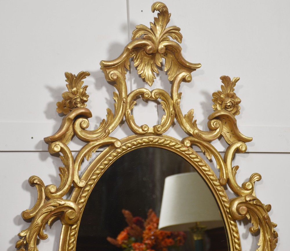 An oval wall mirror set in a gilded frame decorated with carved C-scrolls, floral motifs, and an acanthus leaf crest. View VII