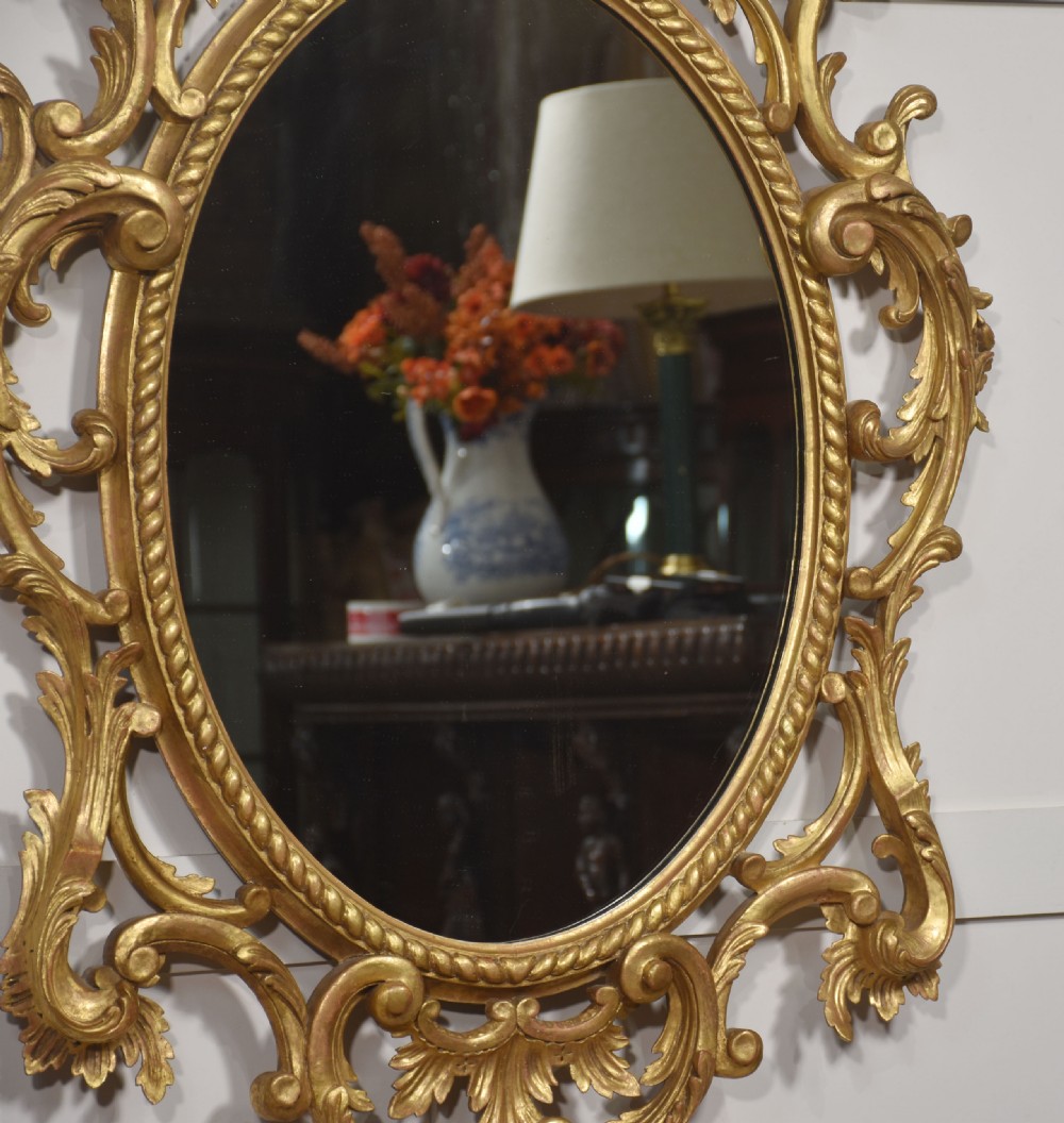 An oval wall mirror set in a gilded frame decorated with carved C-scrolls, floral motifs, and an acanthus leaf crest. View VIII
