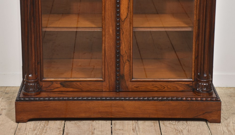 A 19th-century dark rosewood glazed low bookcase featuring two arched glass doors, fluted side pilasters, and carved mouldings. View XVI