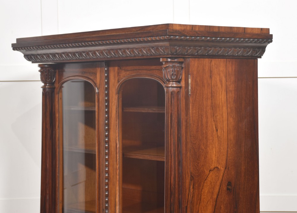 A 19th-century dark rosewood glazed low bookcase featuring two arched glass doors, fluted side pilasters, and carved mouldings. View XX