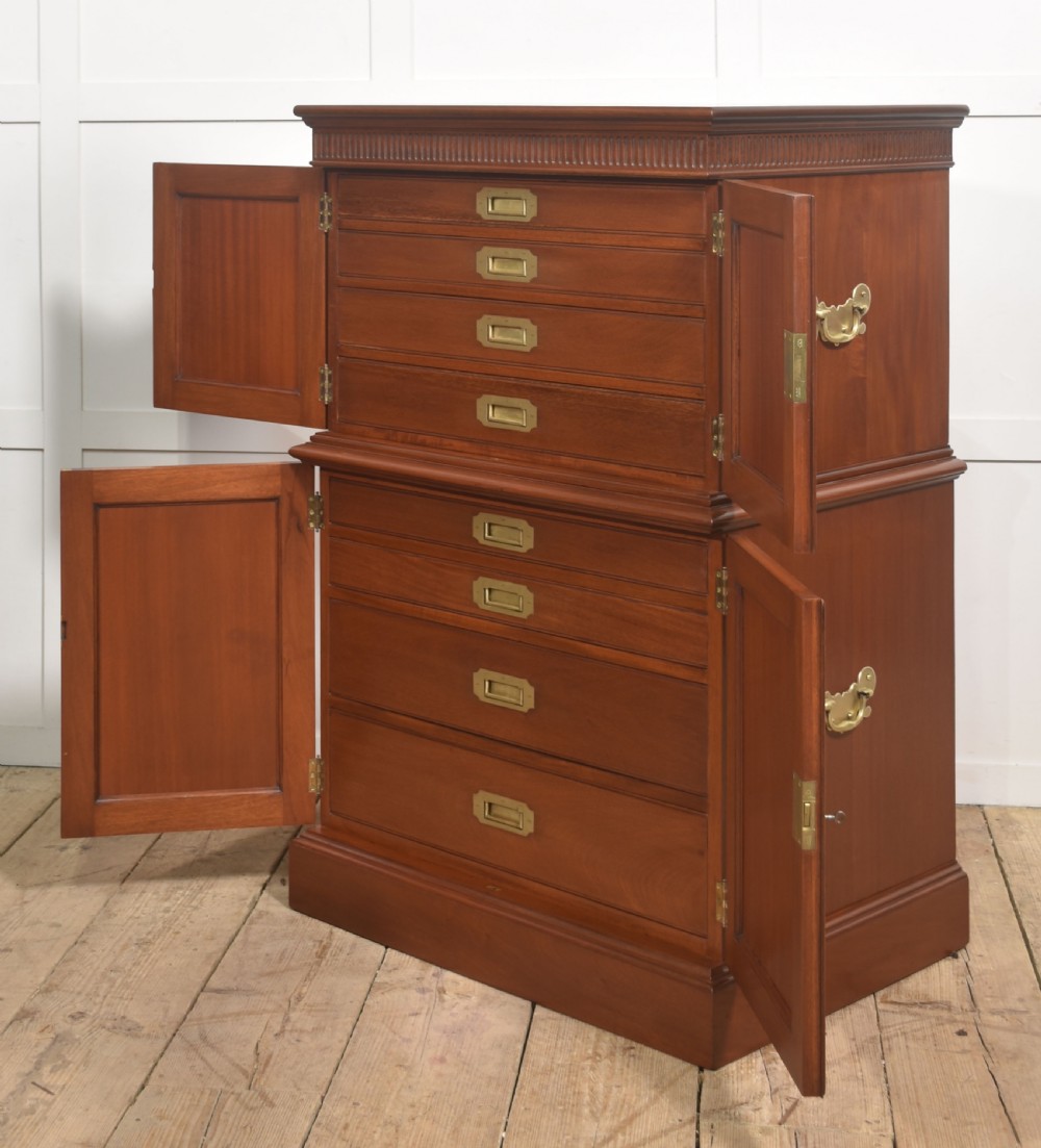 A two-section mahogany collectors cabinet featuring double doors that open to reveal stacked drawers with flush brass handles.