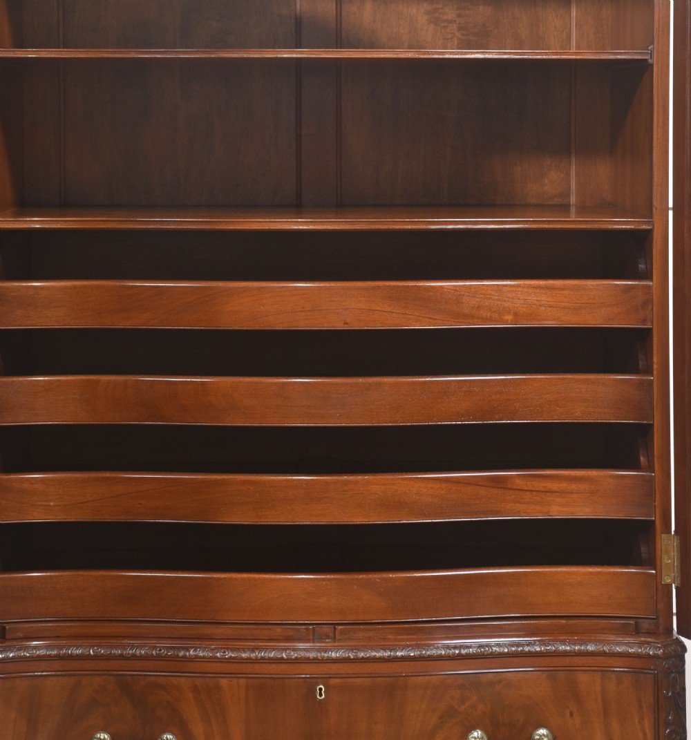 A tall figured mahogany linen press featuring carved corner motifs on double upper doors and two drawers with brass handles below. View III