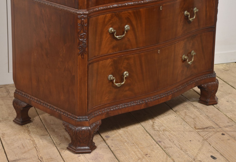 A tall figured mahogany linen press featuring carved corner motifs on double upper doors and two drawers with brass handles below. View VII