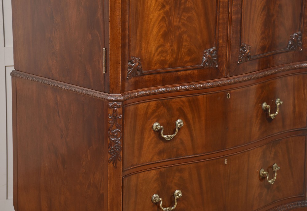 A tall figured mahogany linen press featuring carved corner motifs on double upper doors and two drawers with brass handles below. View VIII