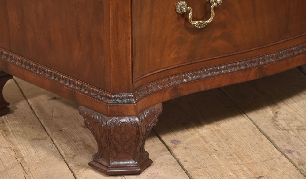 A tall figured mahogany linen press featuring carved corner motifs on double upper doors and two drawers with brass handles below. View X