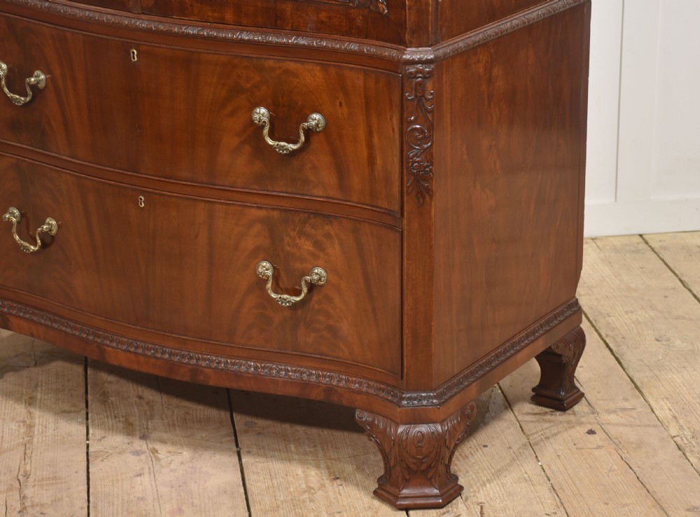 A tall figured mahogany linen press featuring carved corner motifs on double upper doors and two drawers with brass handles below. View XII