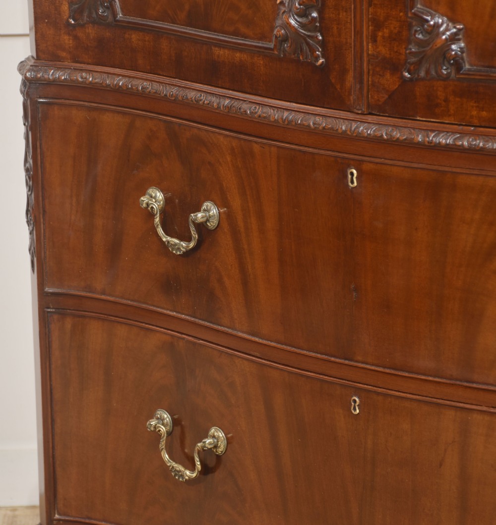 A tall figured mahogany linen press featuring carved corner motifs on double upper doors and two drawers with brass handles below. View XIII