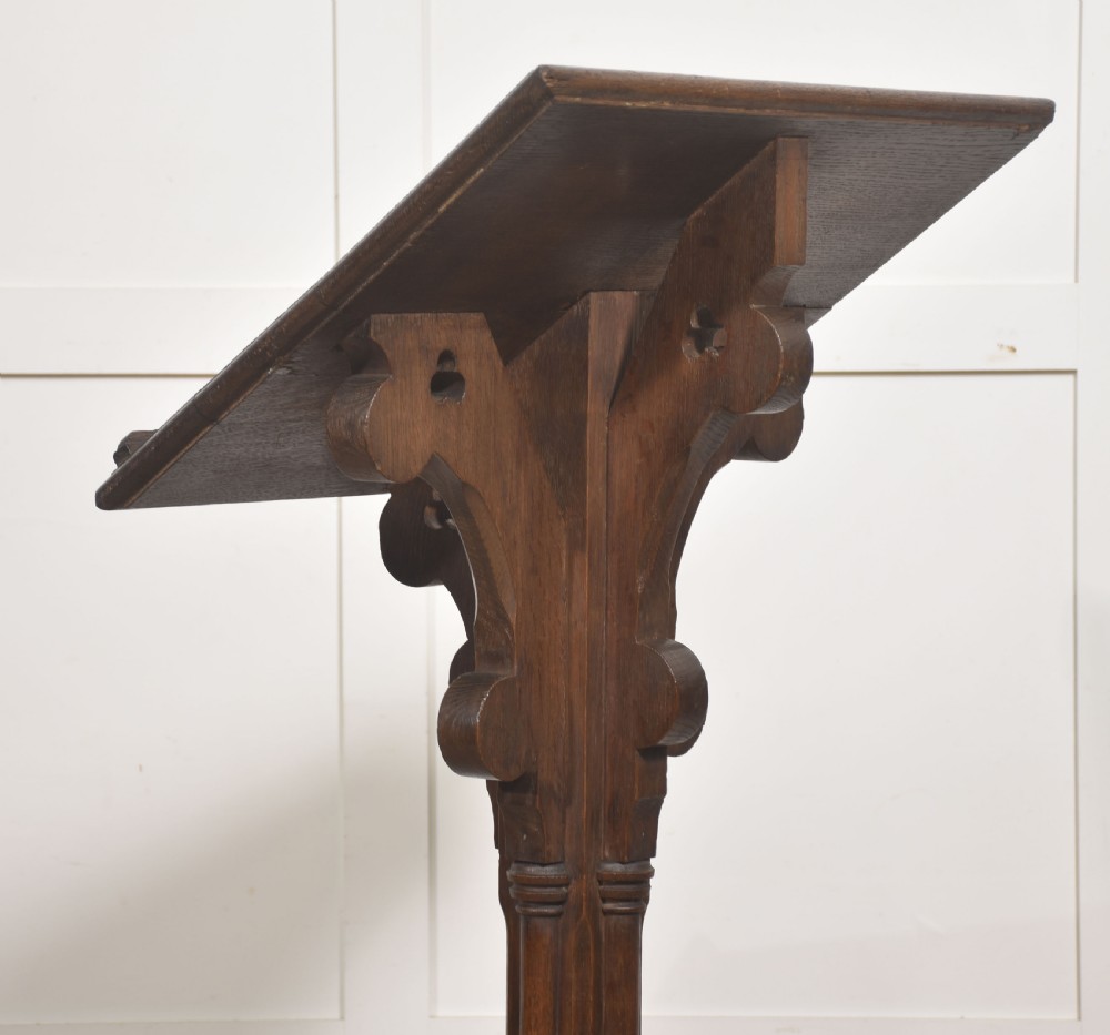 A dark carved oak Gothic Revival lectern stand featuring a sloped top, trefoil cut-outs, a central column, and a four-legged base. View V
