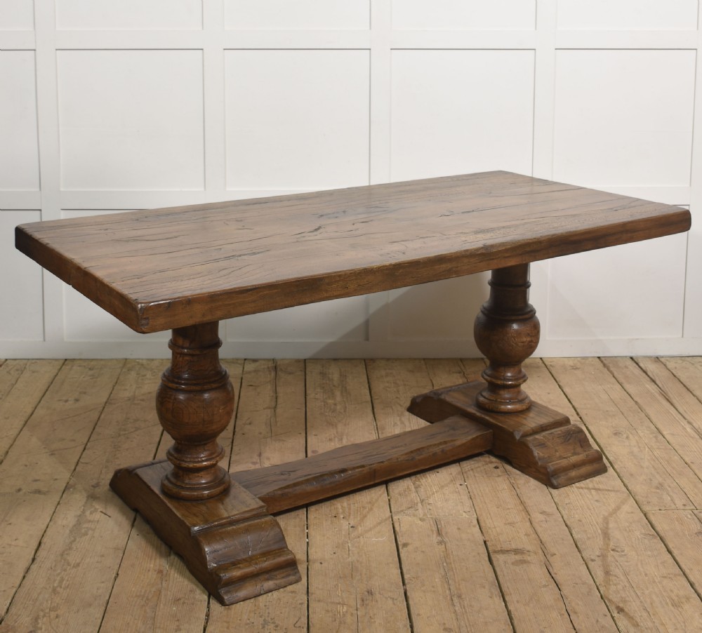 Solid oak refectory dining table featuring thick timber top, bulbous turned baluster pedestals, and a floor stretcher rail.