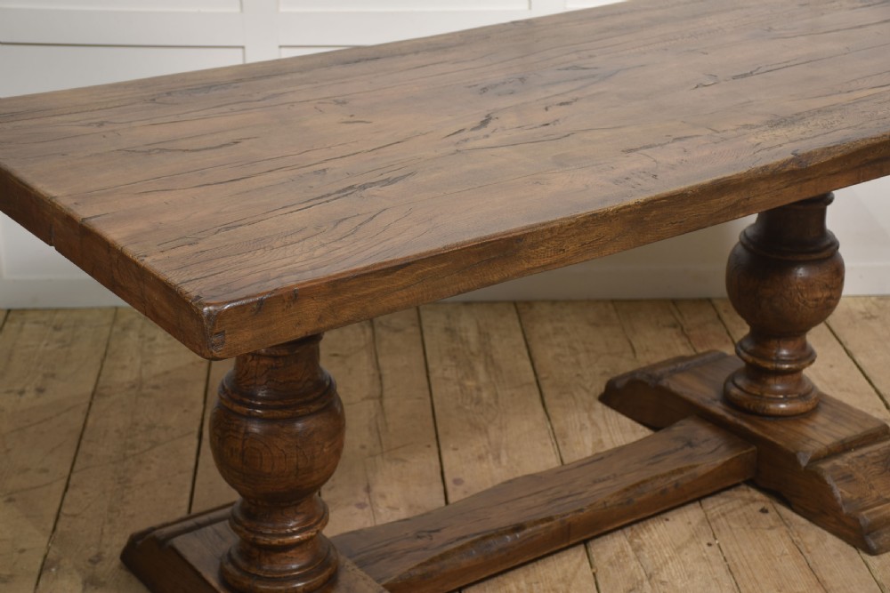 Solid oak refectory dining table featuring thick timber top, bulbous turned baluster pedestals, and a floor stretcher rail. View V