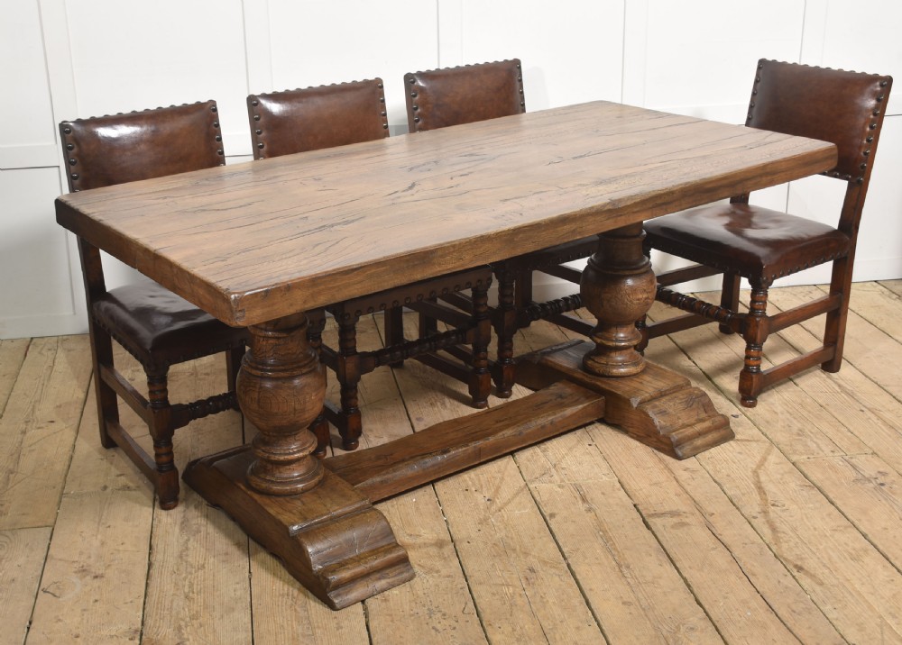 Solid oak refectory dining table featuring thick timber top, bulbous turned baluster pedestals, and a floor stretcher rail. View X