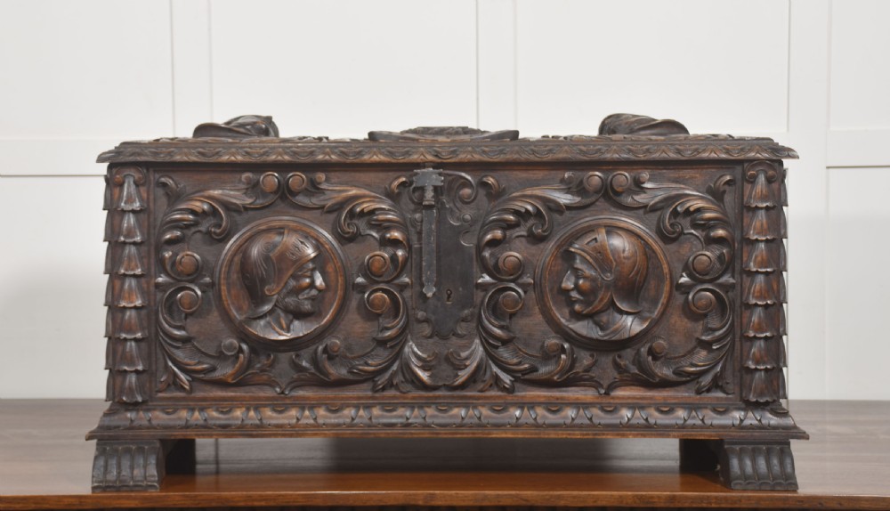 A dark carved walnut coffer featuring two profile portrait medallions surrounded by intricate acanthus foliage carving and a central iron lock plate.