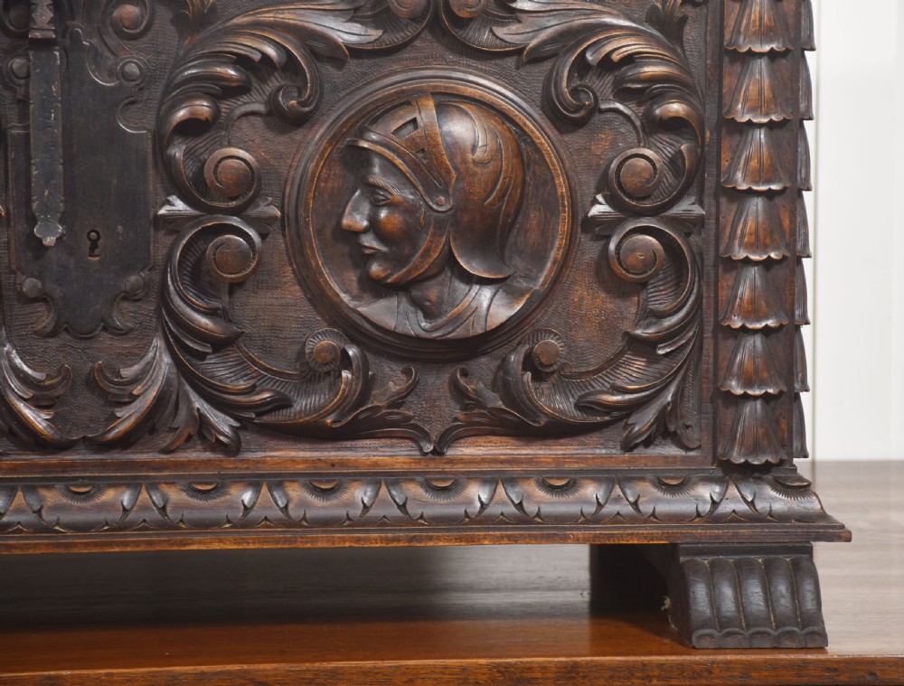 A dark carved walnut coffer featuring two profile portrait medallions surrounded by intricate acanthus foliage carving and a central iron lock plate. View III