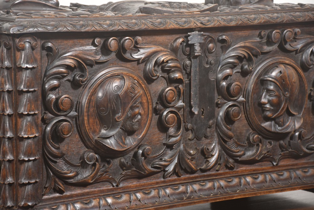 A dark carved walnut coffer featuring two profile portrait medallions surrounded by intricate acanthus foliage carving and a central iron lock plate. View IV