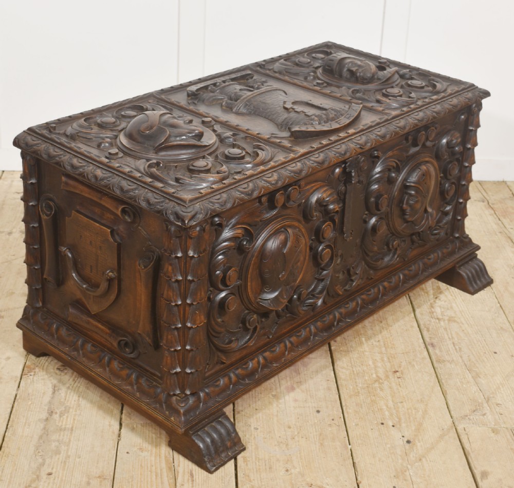 A dark carved walnut coffer featuring two profile portrait medallions surrounded by intricate acanthus foliage carving and a central iron lock plate. View V