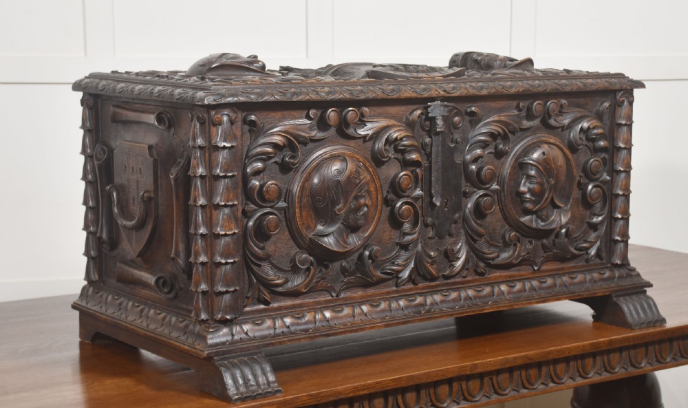 A dark carved walnut coffer featuring two profile portrait medallions surrounded by intricate acanthus foliage carving and a central iron lock plate. View VI