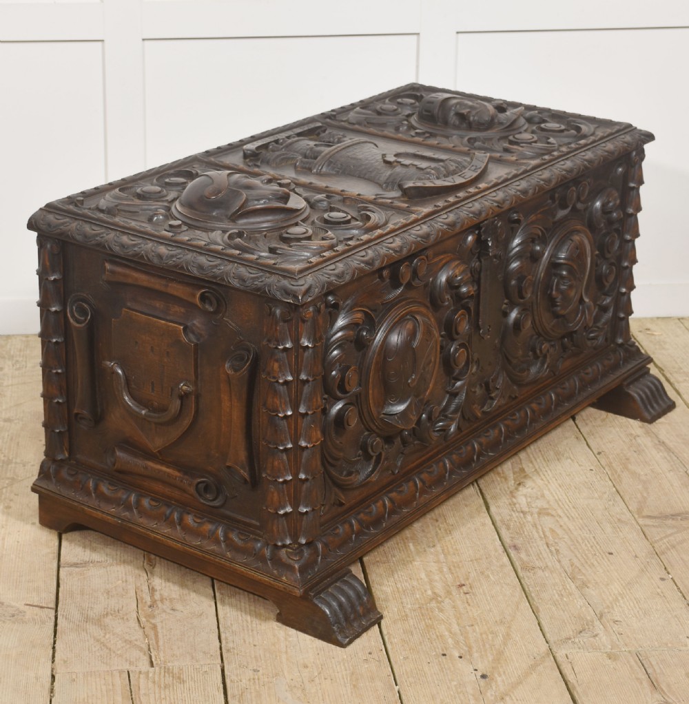 A dark carved walnut coffer featuring two profile portrait medallions surrounded by intricate acanthus foliage carving and a central iron lock plate. View X