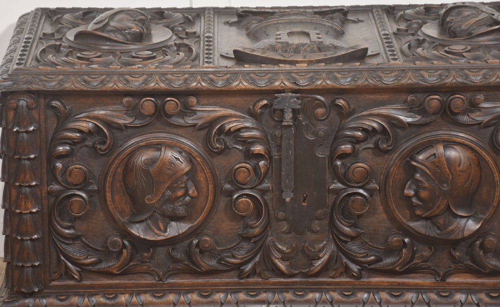 A dark carved walnut coffer featuring two profile portrait medallions surrounded by intricate acanthus foliage carving and a central iron lock plate. View XII