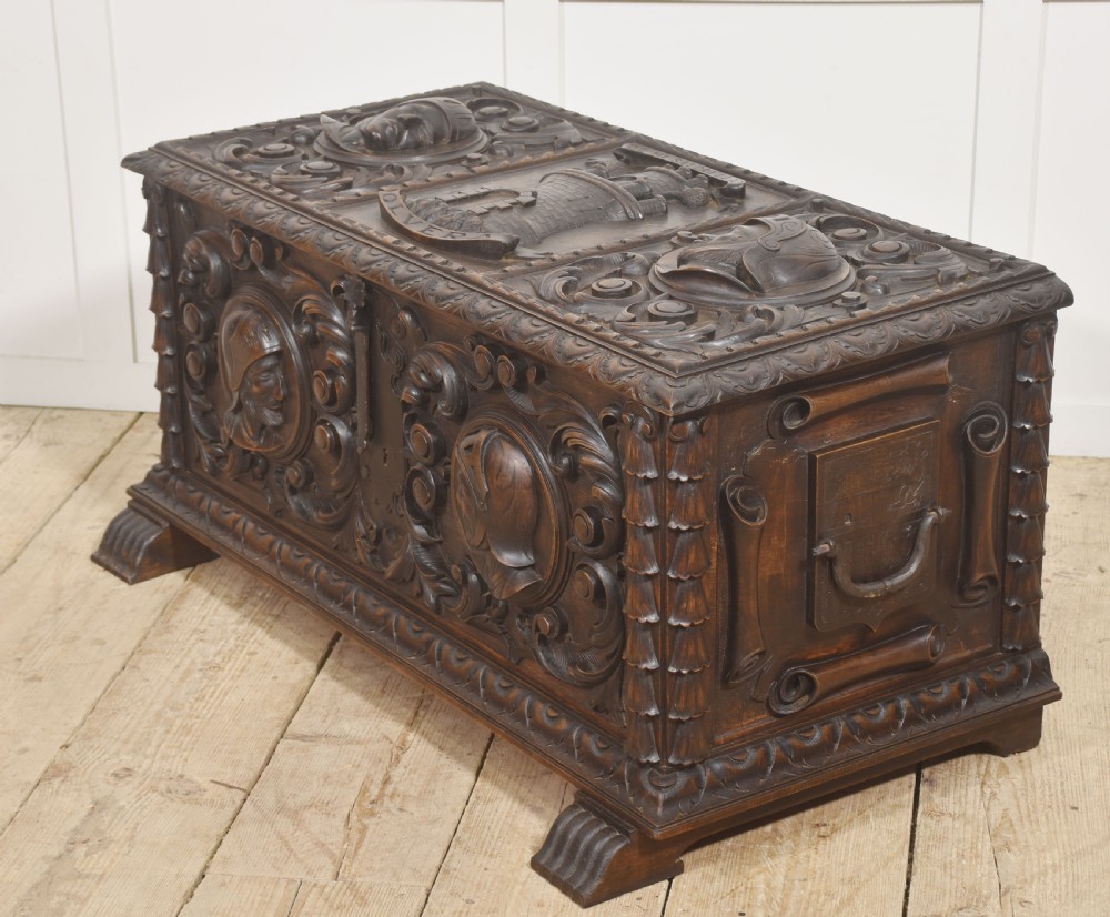 A dark carved walnut coffer featuring two profile portrait medallions surrounded by intricate acanthus foliage carving and a central iron lock plate. View XIII