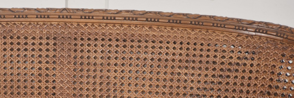 A Louis XVI Revival carved walnut settee featuring a curved woven cane back and a green damask upholstered seat cushion, supported by turned fluted legs. View II