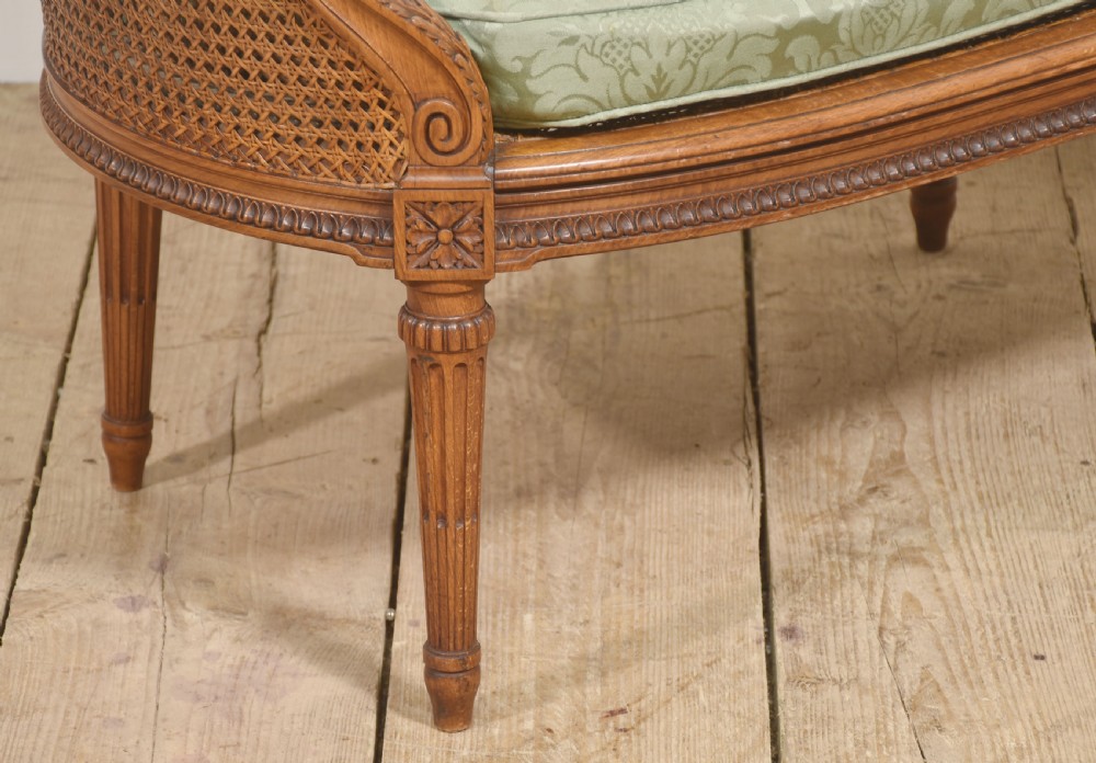 A Louis XVI Revival carved walnut settee featuring a curved woven cane back and a green damask upholstered seat cushion, supported by turned fluted legs. View VII