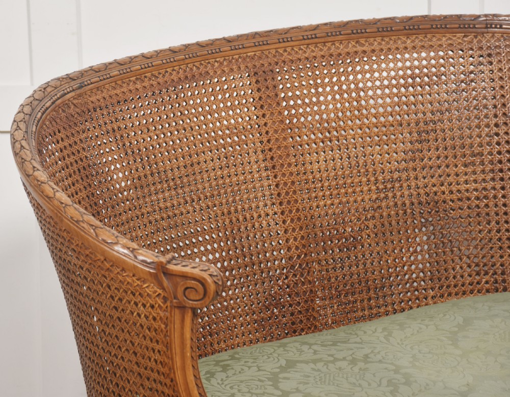 A Louis XVI Revival carved walnut settee featuring a curved woven cane back and a green damask upholstered seat cushion, supported by turned fluted legs. View VIII