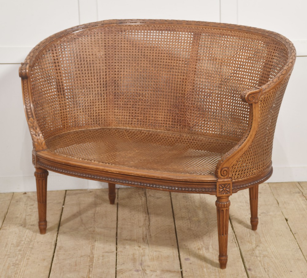 A Louis XVI Revival carved walnut settee featuring a curved woven cane back and a green damask upholstered seat cushion, supported by turned fluted legs. View X