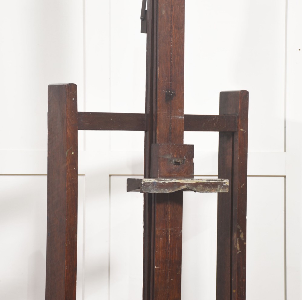 A tall dark oak adjustable artists studio easel featuring a hand-crank winding mechanism and castors. View II