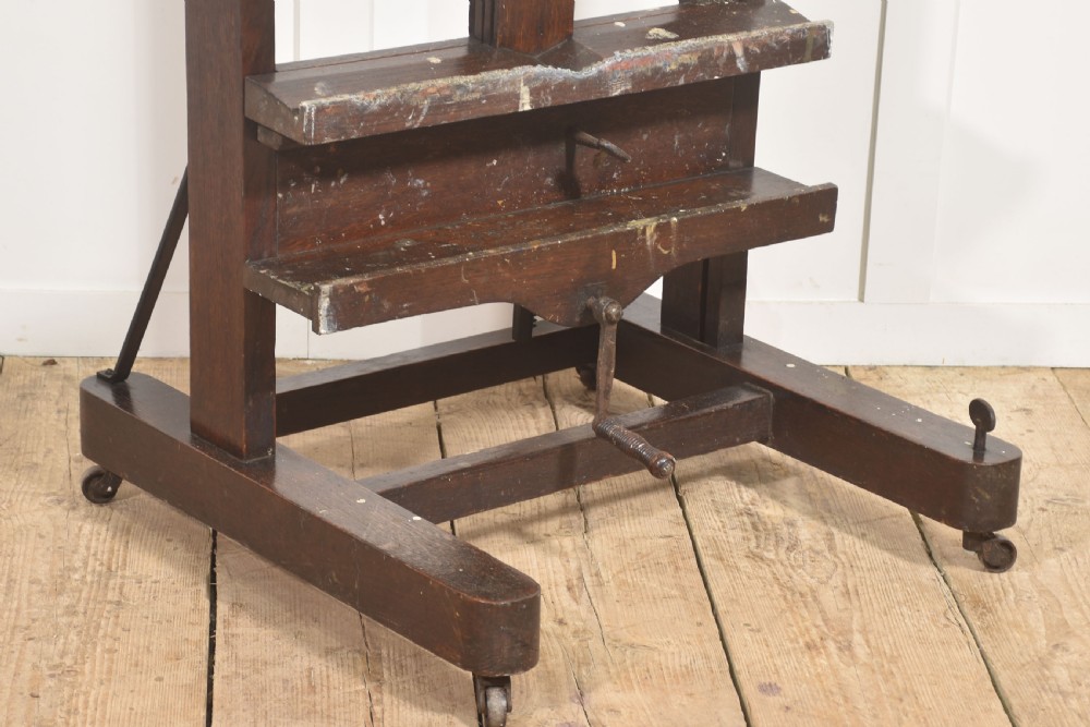A tall dark oak adjustable artists studio easel featuring a hand-crank winding mechanism and castors. View VII