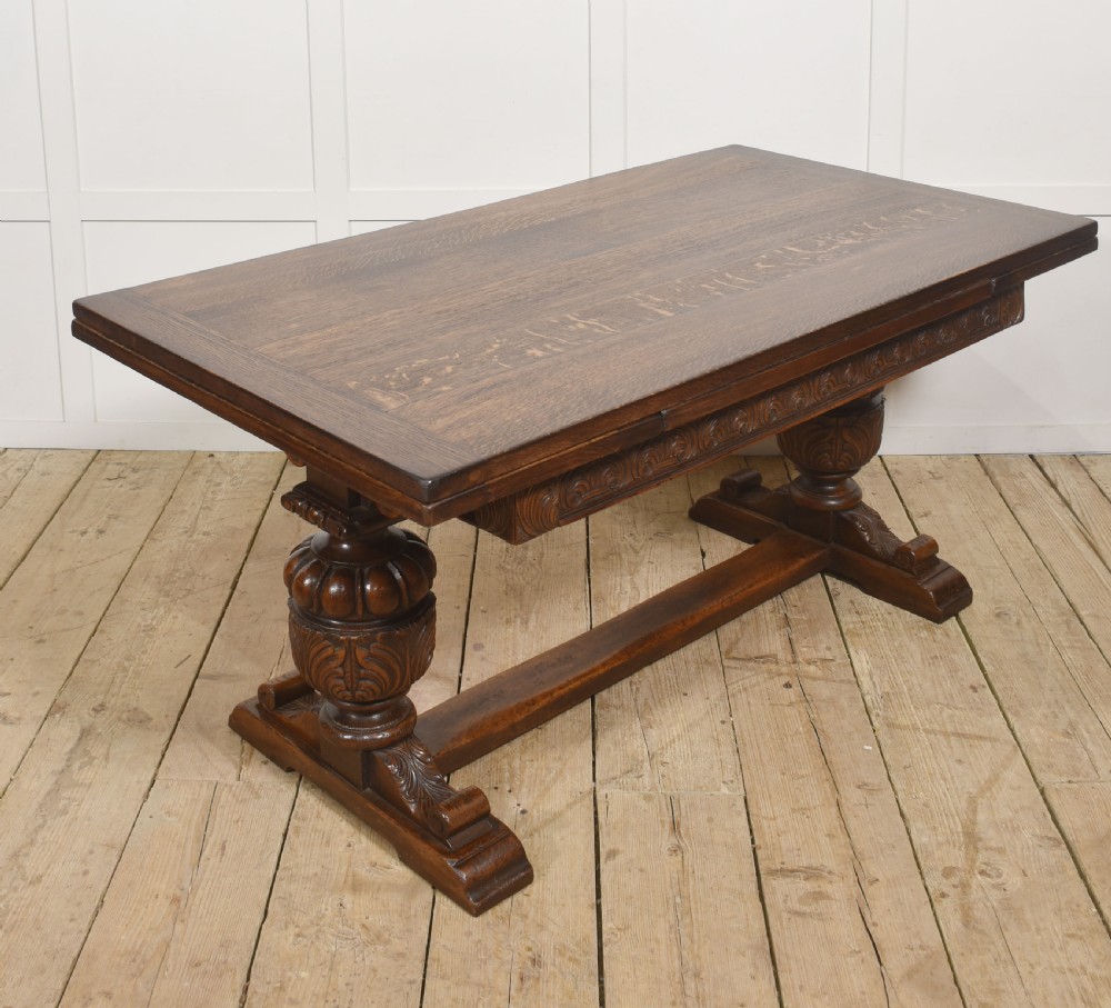 A dark carved oak refectory dining table featuring bulbous turned legs, a carved apron, and pull-out draw-leaf extensions.